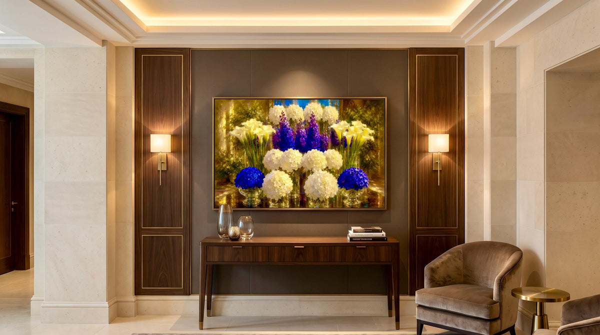 A framed floral wall art piece hangs in a modern, elegant interior hallway above a dark wood console table, flanked by two lit sconces and a gray upholstered armchair.